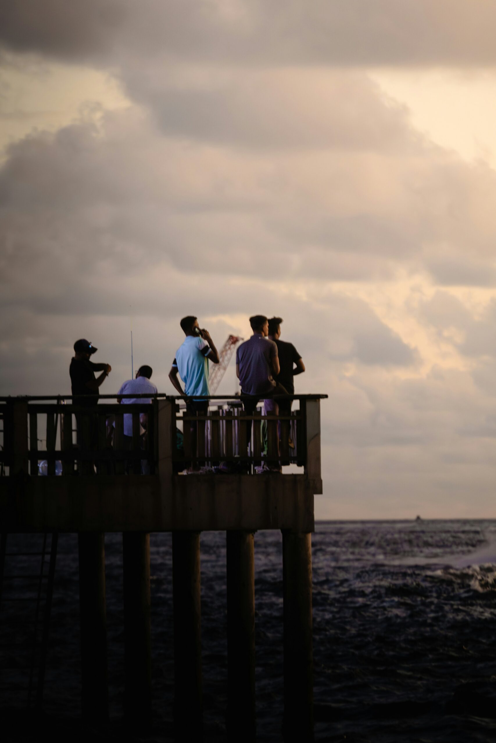 Friends fishing together from a pier at sunset, photographed by Abdhul Masyh